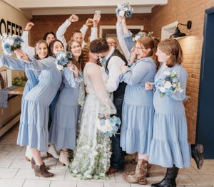 Wedding party celebrating with bride in flowing dress and bridesmaids in light blue dresses.