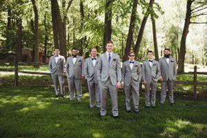 Groomsmen arranged in triangle formation wearing matching light gray suits in outdoor garden setting.