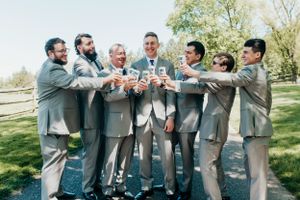 Wedding party in gray suits toasting with drinks during an outdoor celebration.