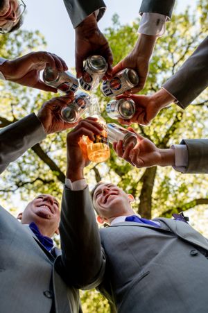Low angle shot of hands clinking beer bottles together in a circle against a sunlit sky.