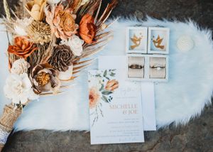 Wedding invitation suite with dried flowers and peach-colored blooms on a fuzzy blue backdrop.