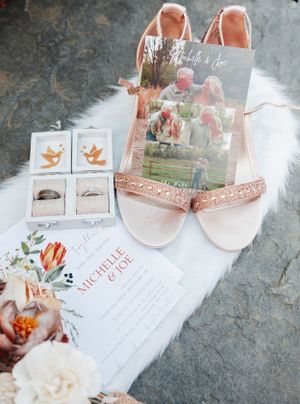 Wedding details including pink shoes, invitation, and photographs arranged on white fur.
