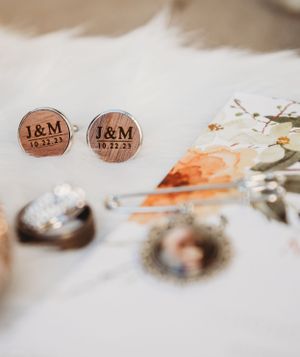 Custom wooden cufflinks with initials J&M and date displayed alongside floral wedding details.