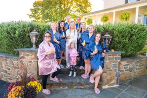Wedding party in coordinated blue robes gathered on stone steps outside a country house.