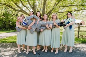 Bridesmaids in sage green dresses playfully carrying groomsmen in matching suits outdoors.
