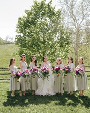 Wedding party with bridesmaids in sage dresses holding vibrant purple and pink bouquets.