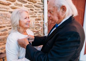 An elegantly dressed couple sharing an intimate moment against a rustic stone wall.