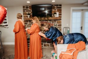 People in orange and navy dresses preparing in a room with exposed brick and mounted TV.