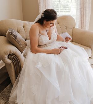 Bride in lace wedding dress sitting on beige couch looking at phone.