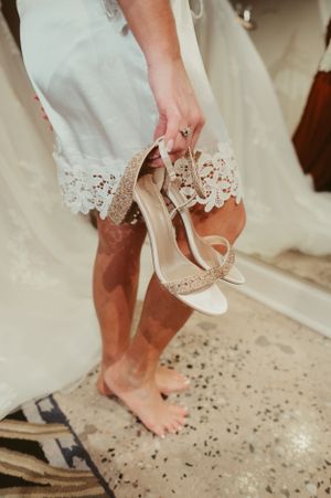 Close-up of sparkly white wedding heels being held against a lace dress hem.