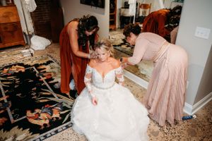 Final wedding preparations with bridesmaids helping with dress and accessories.