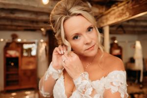 Bride getting ready in a rustic venue with exposed wooden beams and warm lighting.