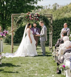 Outdoor wedding ceremony under wooden arch decorated with pink and white flowers.