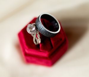 Wedding rings displayed on a red velvet ring box, featuring a black band and diamond engagement ring.