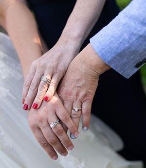 Close-up of newlyweds' hands displaying wedding rings and red nail polish.