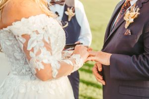 Close-up of wedding ceremony ring exchange with lace dress details in an outdoor setting.