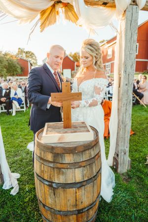 Wedding ceremony at rustic venue with wooden barrel altar and cross under draped fabric canopy.