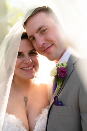 Close up wedding portrait of a couple smiling in sunlight with the groom wearing a gray suit and floral boutonniere.