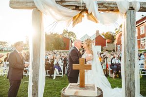 Sunset wedding ceremony under white draped canopy with wooden barrel altar and cross.