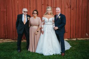 Wedding party poses in front of red barn on sunny afternoon.