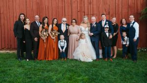 Large wedding party group photo against rustic red barn backdrop.