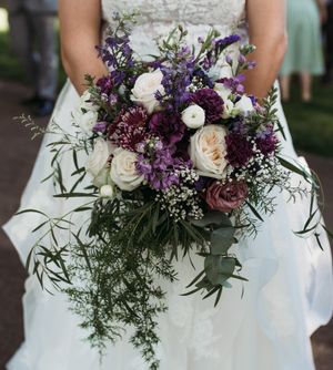 Cascading bridal bouquet with purple, white and mauve roses with delicate greenery.