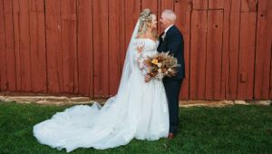 Wedding couple poses together against rustic red barn backdrop in outdoor countryside setting.