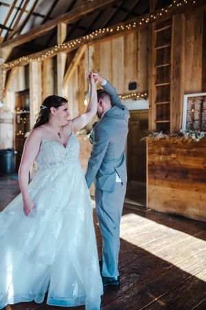 Wedding couple dancing in rustic barn venue with twinkling lights.