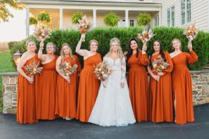 Wedding party celebrates with joyful poses outside elegant white house with porch.