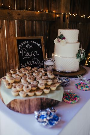 Wedding dessert table featuring a white cake and pecan tarts display with colorful candies in a rustic setting.