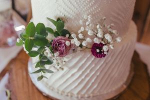 Wedding cake detail showing delicate white frosting decorated with purple flowers and baby's breath.