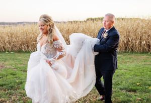 Couple shares playful moment in cornfield as wedding dress catches breeze at sunset.