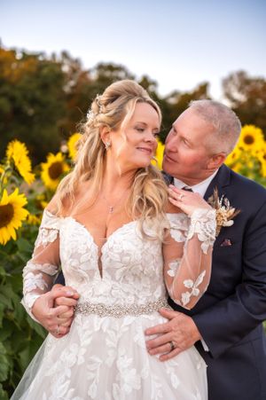 Romantic wedding portrait in a sunflower field at sunset with a stunning lace dress and elegant navy suit.
