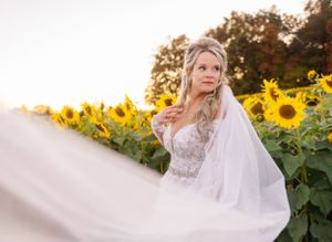 Ethereal bridal portrait with flowing veil against vibrant sunflower field at golden hour.