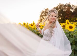 Dreamy sunlit wedding photo with flowing veil and sunflower backdrop.