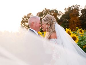 Romantic sunset portrait in sunflower field with flowing white veil.