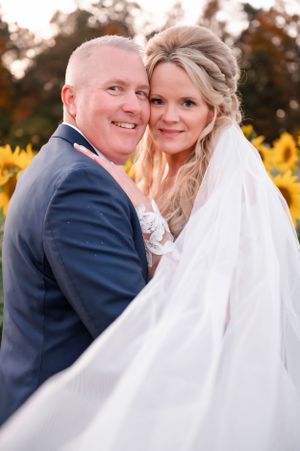 Joyful wedding portrait in front of sunflower field during golden hour.