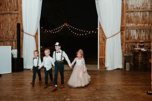 Children in formal attire dancing during rustic barn wedding reception.