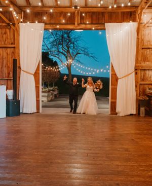 Wedding celebration in rustic barn venue with string lights and white curtains framing the entrance.