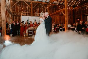 First dance in barn venue with dramatic fog effect and string lights overhead.