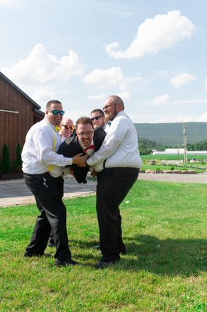 Groomsmen playfully pose for a fun group photo outside a rustic barn.