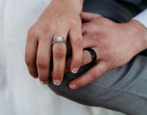 Close-up of wedding rings with bride wearing diamond engagement ring and groom wearing black band.