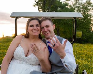 Newlyweds showing off their wedding rings while seated in a golf cart at sunset.