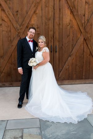 Wedding portrait of a couple in formal attire against a rustic wooden barn backdrop.