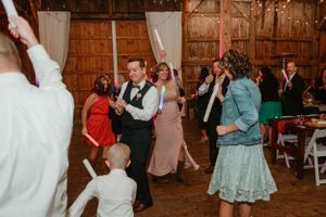Wedding reception dance party in a rustic barn with string lights and wooden beams.