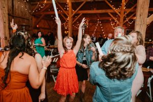 Wedding guests dance and celebrate at a rustic barn reception decorated with string lights.