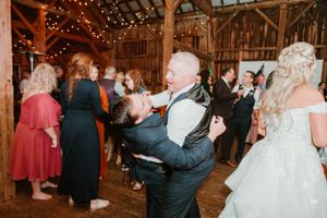 Wedding celebration features lively dancing in rustic barn decorated with twinkling lights.