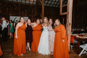 Wedding party poses in orange bridesmaid dresses inside rustic barn reception venue.