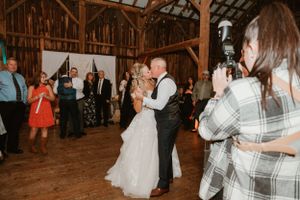 Wedding couple dances while guests capture moments in rustic barn venue.