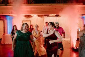 Wedding guests dance enthusiastically under red and blue lighting at an indoor reception party.